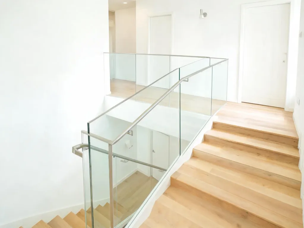Nowoczesne, jasne schody z szklaną balustradą, bezpiecznym spocznikiem i minimalistycznym korytarzem na piętrze